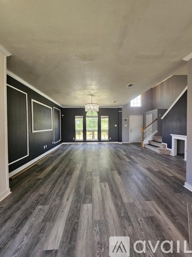 A spacious room with wooden flooring and a staircase on the right side.