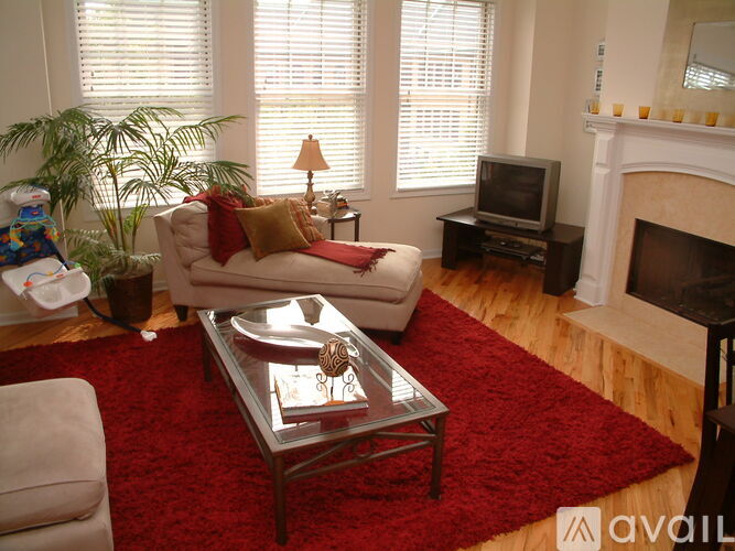 A living room with a red rug and a glass coffee table.