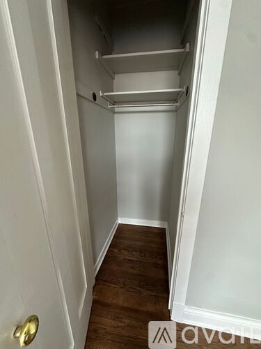 A white door with a gold handle is open to a white hallway with a wooden floor.