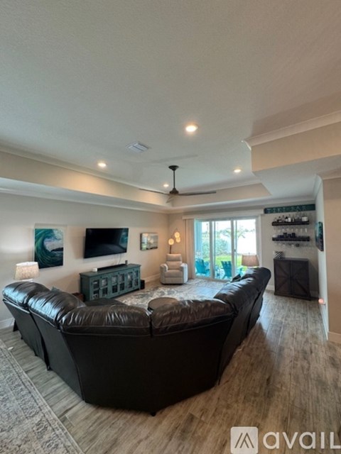 A living room with a black leather sofa and a television on the wall.