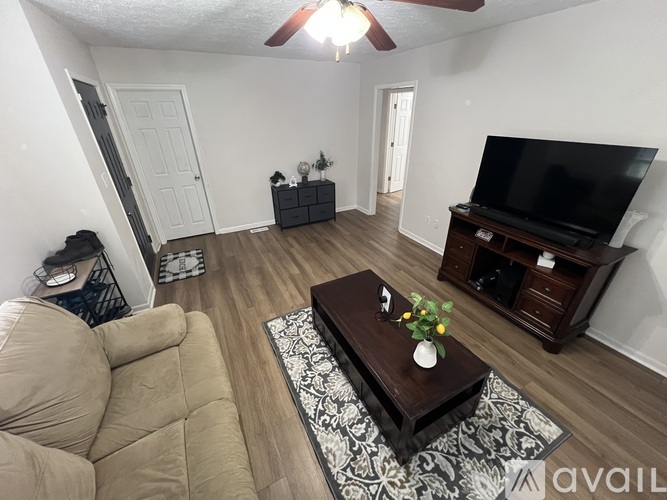 A living room with a tan couch, a coffee table with flowers, and a television on a wooden stand.