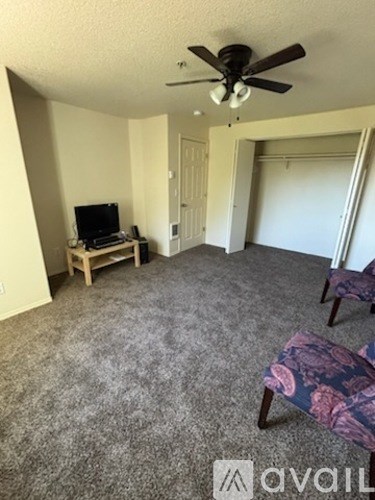 A living room with a grey carpet and a ceiling fan.