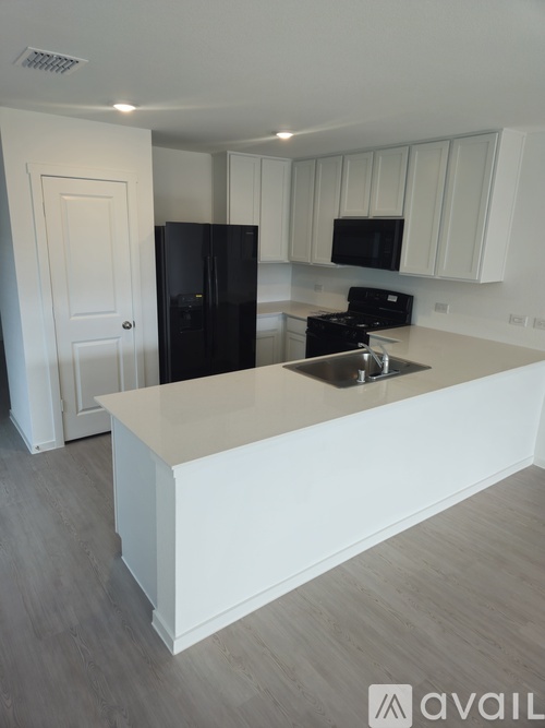 A kitchen with white cabinets and a black fridge.