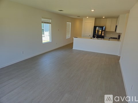 A spacious empty room with wooden flooring and a kitchen area in the background.