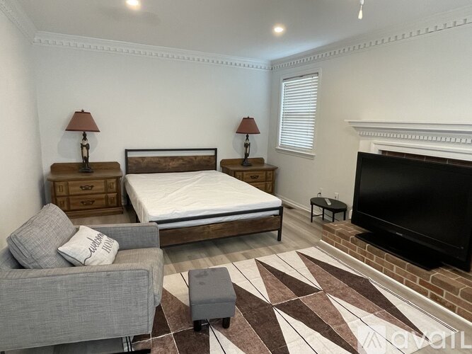 A bedroom with a large bed, a grey couch, and a fireplace.