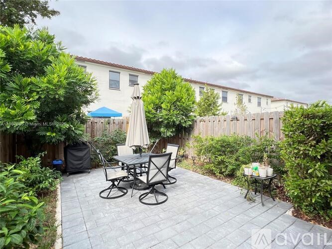 A patio with a table and chairs is surrounded by greenery.