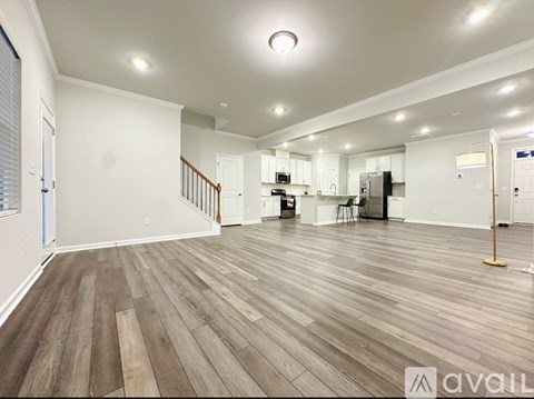 A spacious living room with wooden flooring and a kitchen area in the background.