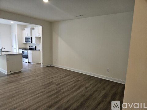 A spacious room with wooden flooring and a kitchen area with white cabinets and appliances.