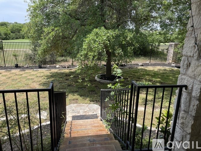 A black metal fence surrounds a stone pillar and a tree in a grassy area.