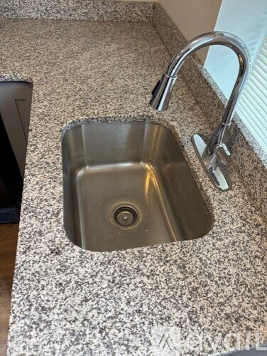 A stainless steel sink with a chrome faucet on a speckled countertop.