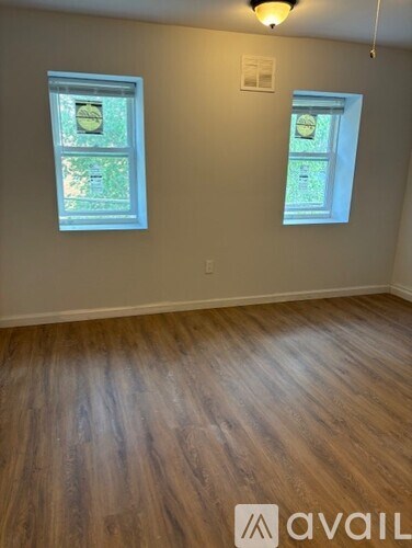 A room with wooden flooring and two windows.