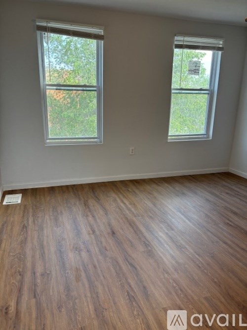 A room with wooden flooring and two windows.