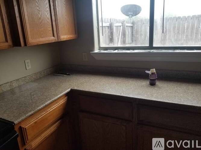 A kitchen counter with wooden cabinets and a window overlooking a fence.
