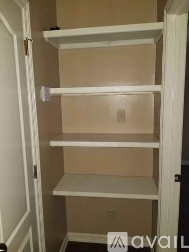 A white shelving unit with four shelves is in a room.