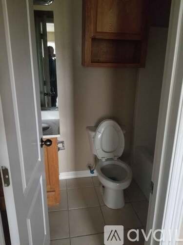 A white toilet in a small bathroom with a wooden cabinet above it.