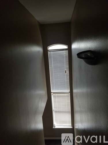 A window with blinds is seen through a narrow opening in a dark room.