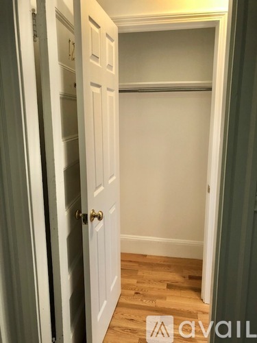 A white door with a gold handle is open to a room with a wooden floor.
