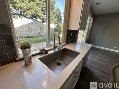 A kitchen with a sink and a window overlooking a backyard.