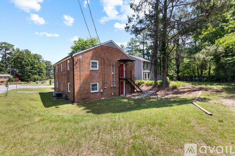 A red brick building with a red door is surrounded by green grass and trees.