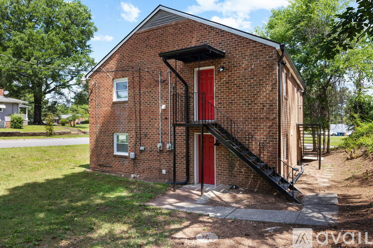 A small red brick house with a black metal staircase leading to a red door.