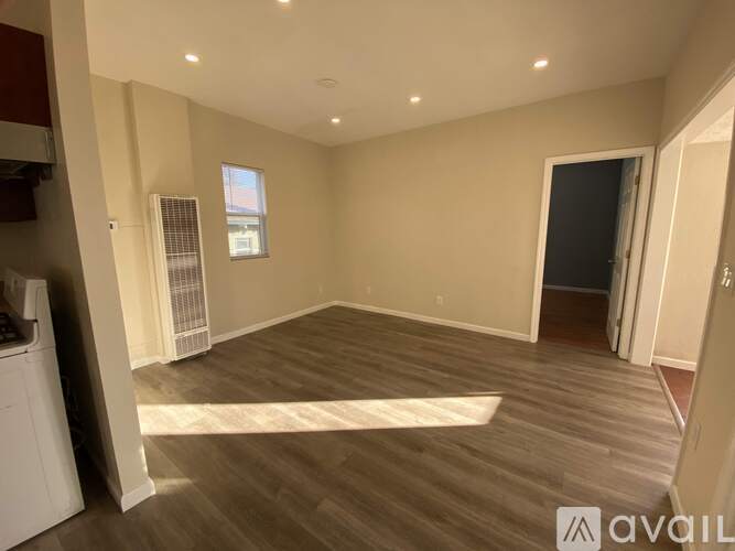 A spacious room with wooden flooring and a window with blinds.