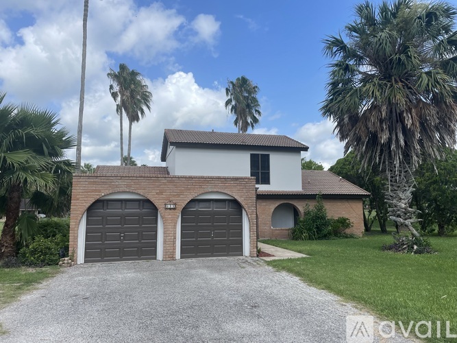A house with two garage doors is surrounded by palm trees.