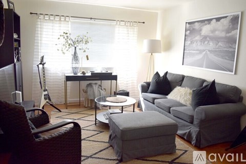 A living room with a grey couch, a chair, a table with a vase of flowers, and a guitar leaning against the wall.