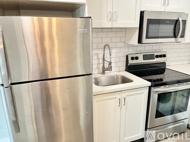 A stainless steel refrigerator is in a kitchen with white cabinets and a black stove.