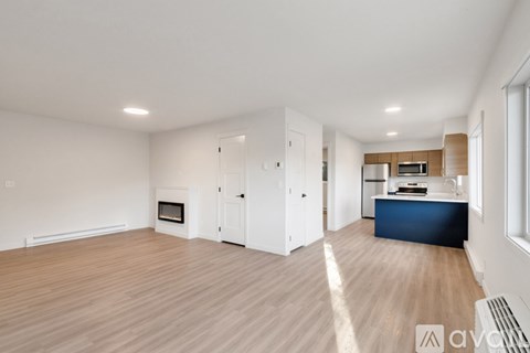 A spacious living room with a fireplace and a kitchen area in the background.