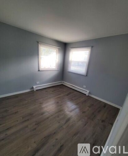 A room with wooden flooring and two windows.