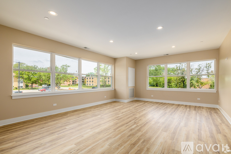 A spacious room with wooden flooring and large windows overlooking a street.