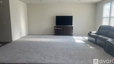 A living room with a grey carpet, a black leather sofa, a wooden cabinet, and a flat screen TV.