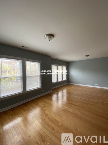 A spacious room with wooden flooring and large windows.
