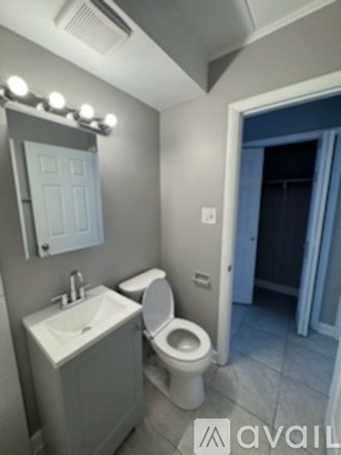 A bathroom with a toilet, sink, mirror, and lights.