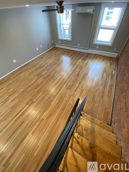 A room with wooden flooring and a staircase leading to another room.