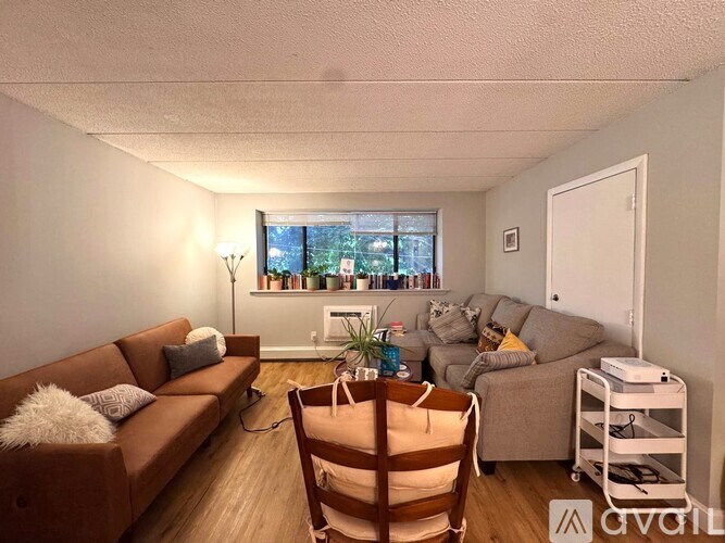 A living room with a brown chair, a brown couch, a brown armchair, a white rug, and a window with a view of trees.