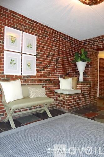 A living room with a white couch and a plant on a brick wall.
