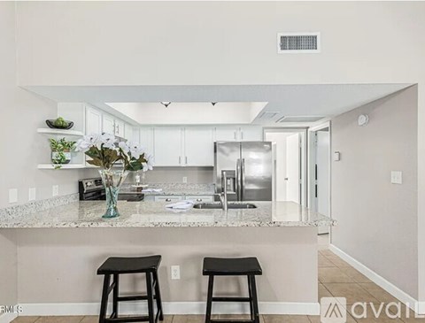 A kitchen with a marble countertop and two black barstools.
