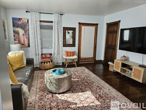 A living room with a rug, a sofa, a chair, a table, a television, and a painting on the wall.