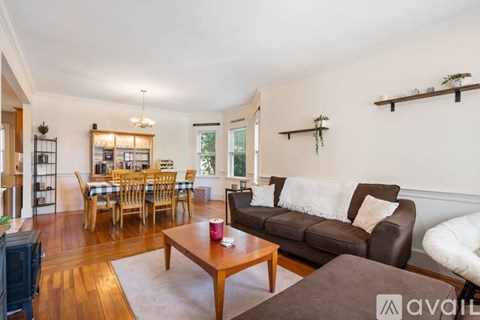 A living room with a brown couch, a wooden coffee table, and a dining table with chairs.