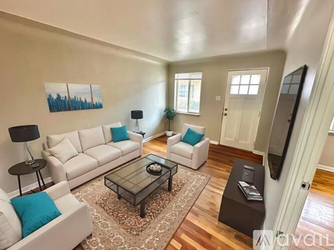 A living room with a white couch, a glass coffee table, and a painting on the wall.