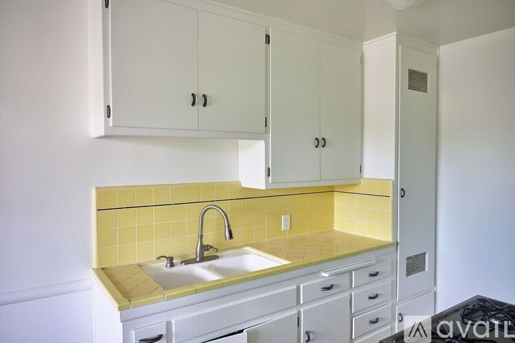 A kitchen with white cabinets and yellow tiles.