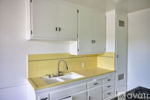 A kitchen with white cabinets and yellow tiles.