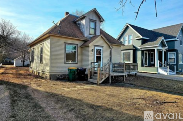 A house with a brown roof and a green trash can in front of it.