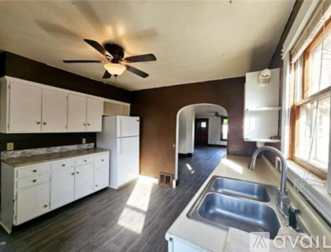 A kitchen with a fan on the ceiling and a sink with two faucets.