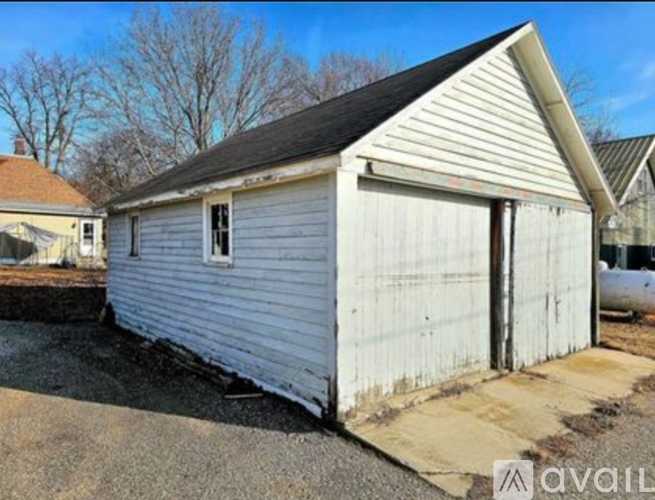A small white building with a black roof is situated in a gravel lot.