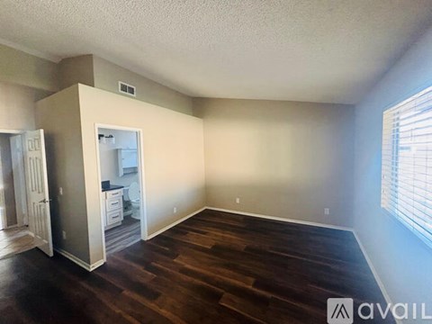 A room with wood flooring and a kitchen visible through the open door.