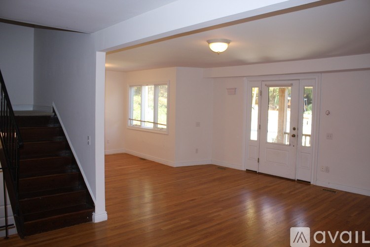 A spacious room with wooden floors and a staircase on the left side.