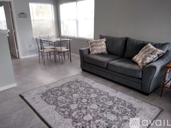 A grey couch with two pillows sits in a living room with a rug and a dining table.