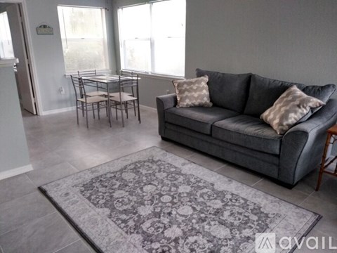 A grey couch with two pillows sits in a living room with a rug and a dining table.